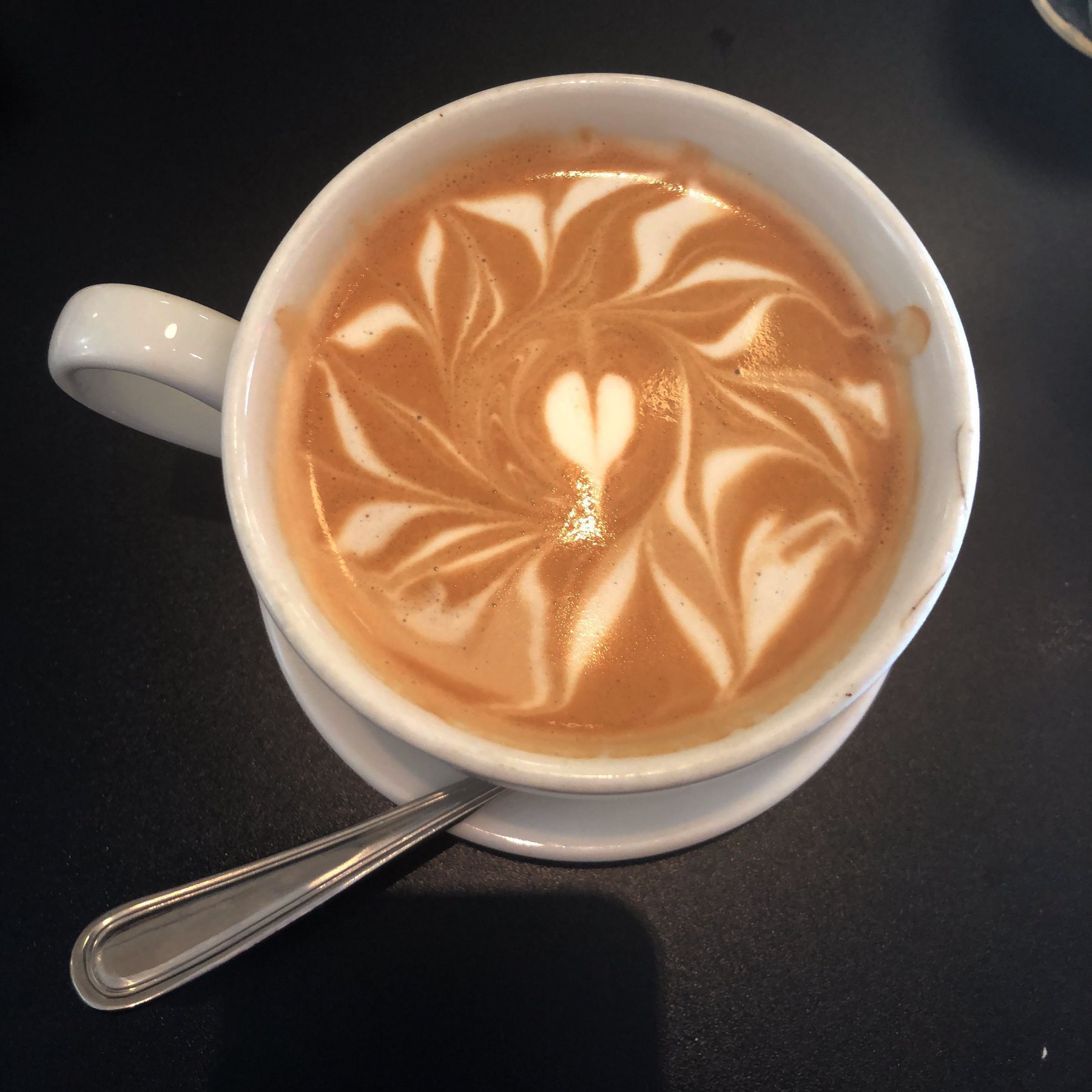 Latte with a heart in the middle, surrounded by swiggles.